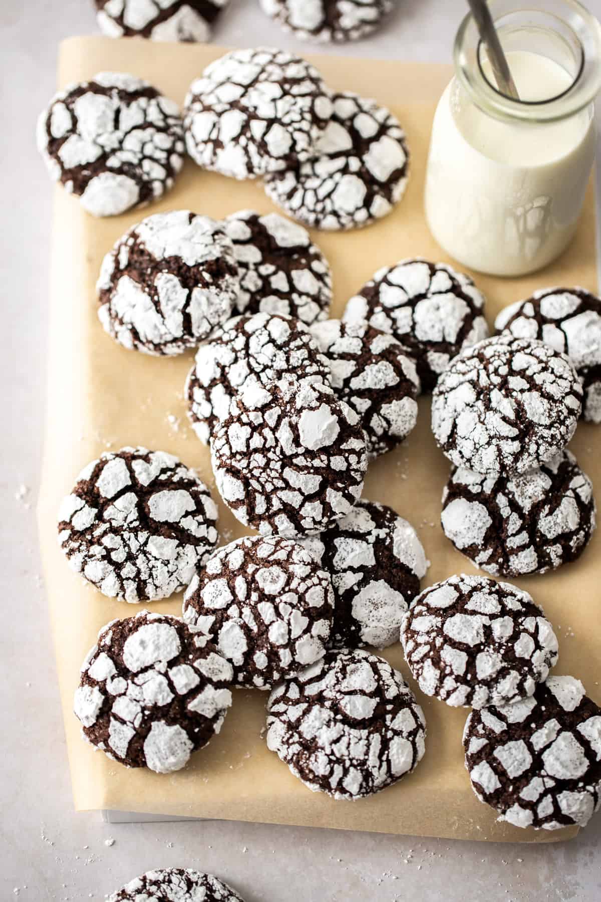 pile of chocolate crinkle cookies on a cutting board with glass of milk and straw