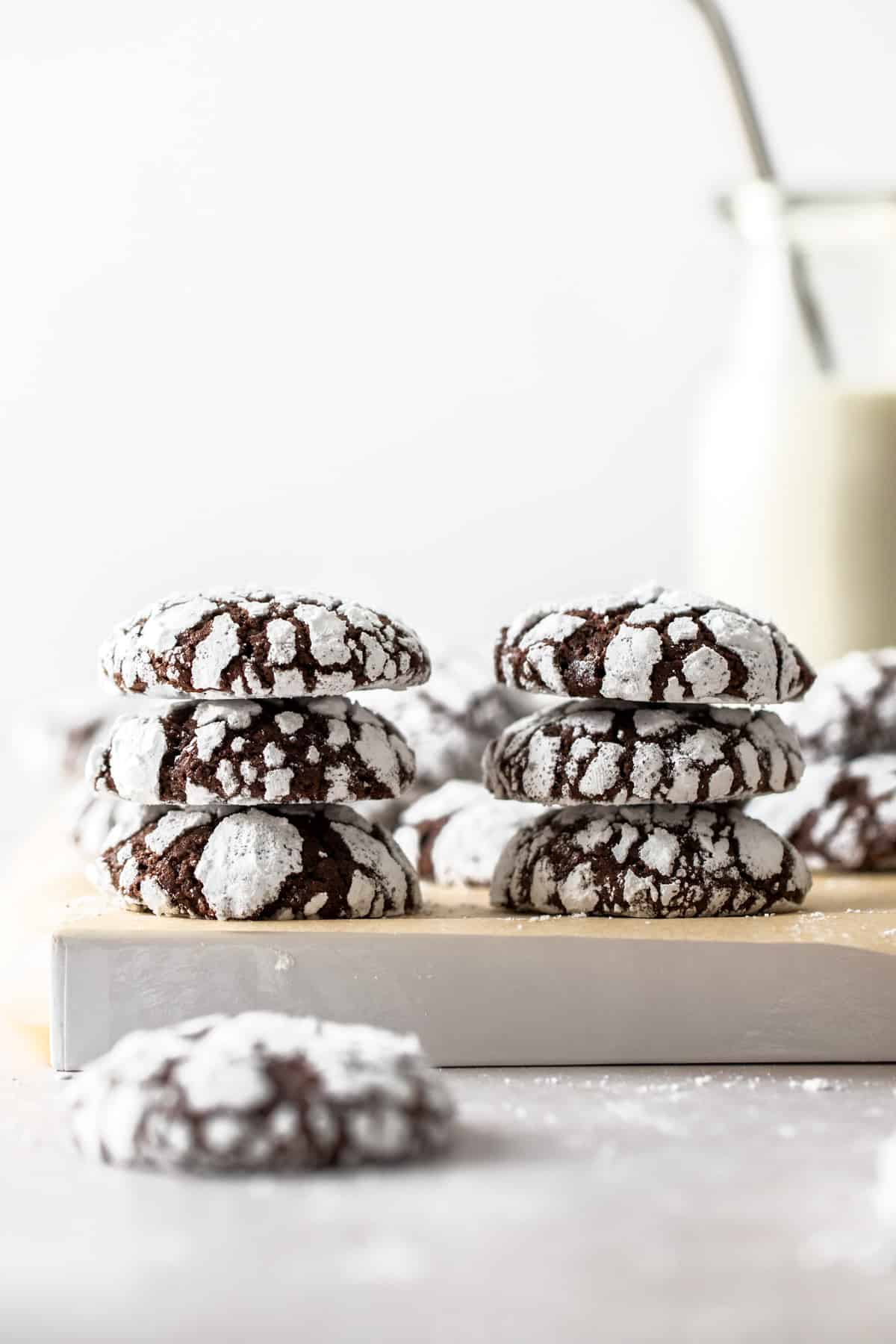 stacks of chocolate crinkle cookies with glass of milk in background