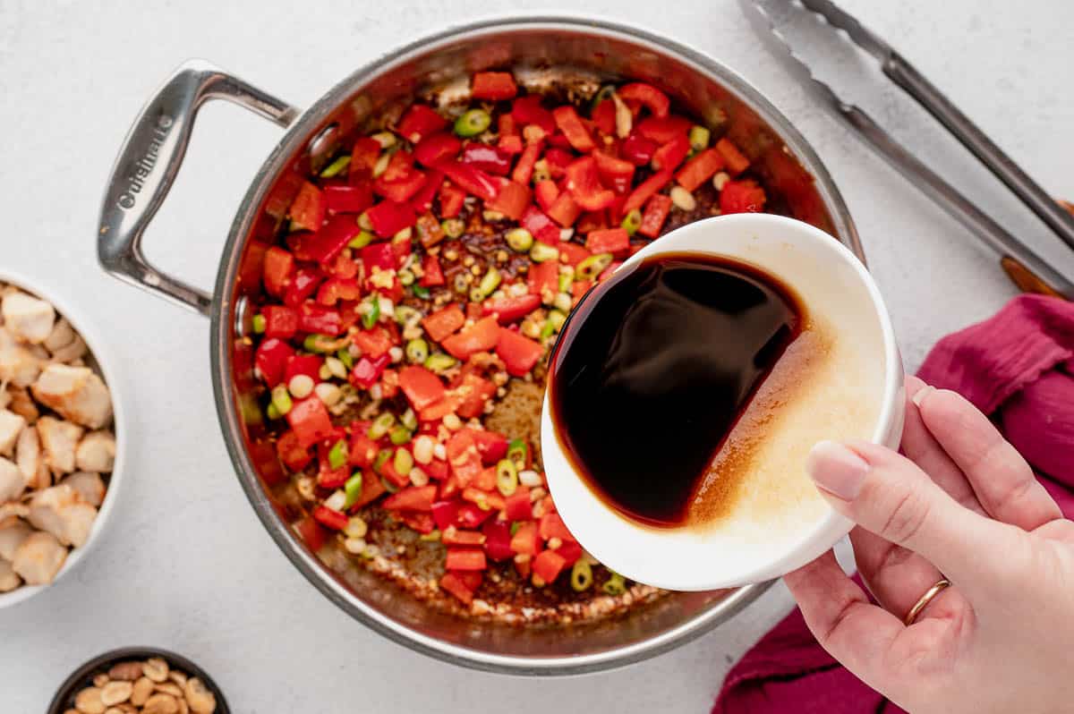 pouring kung pao sauce into pan of veggies