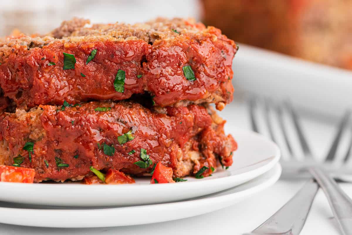 two slices of meatloaf on serving plates with forks
