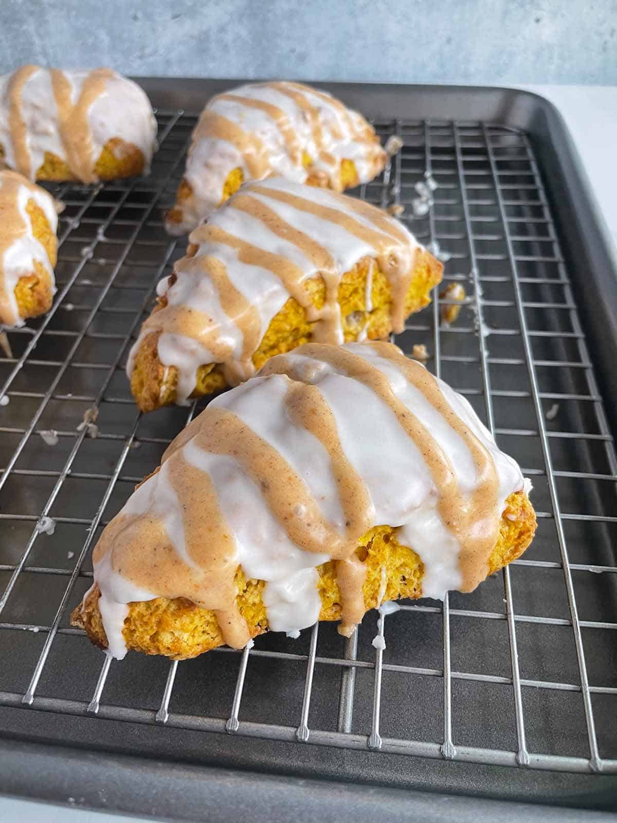 pumpkin scones with icing on a baking sheet with rack