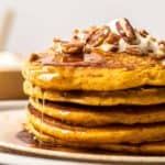 stack of pumpkin spice pancakes with maple syrup and pecans