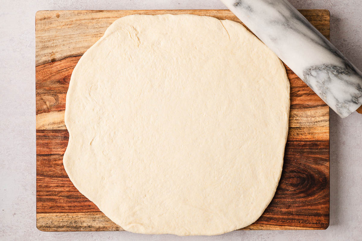 pizza dough rolled into circle on wooden cutting board for chicago style pizza