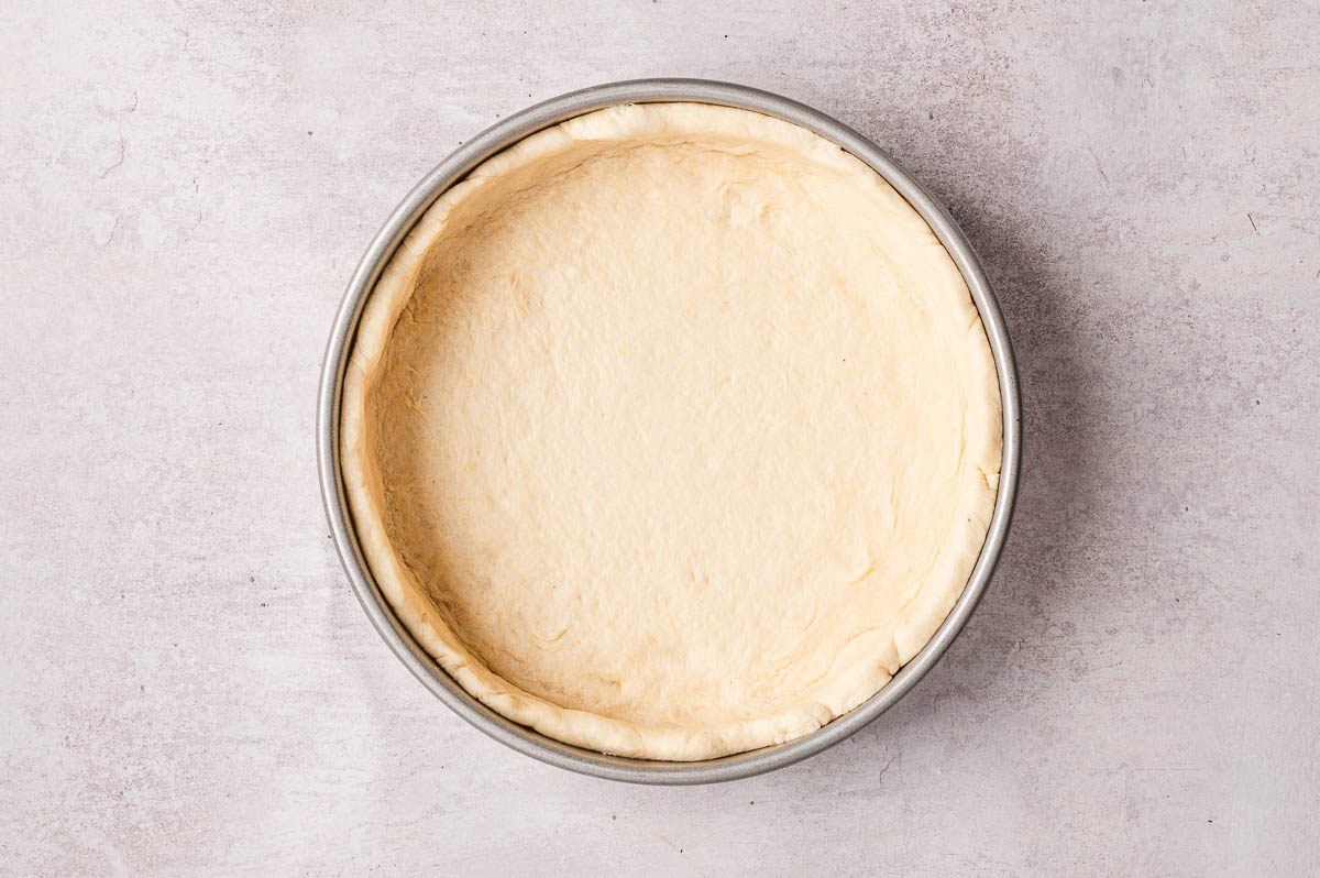 dough pressed into round cake pan for chicago style pizza