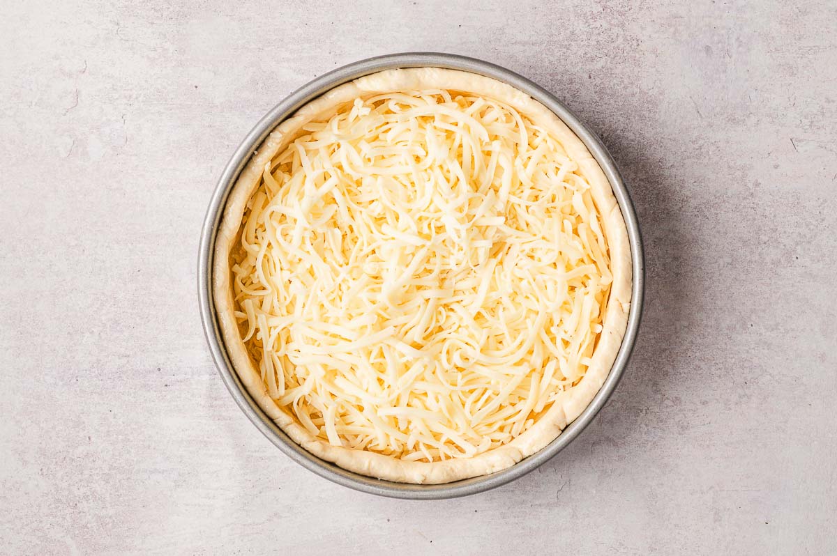 shredded cheese in dough lined cake pan for chicago style pizza recipe