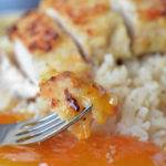 A fork with coconut crusted chicken with apricot sauce on a plate with rice.