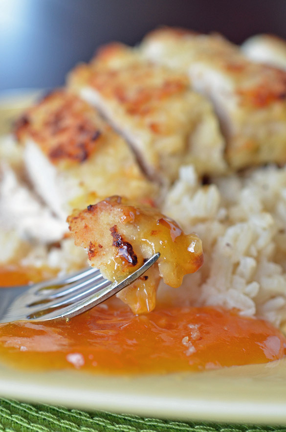 A fork with coconut crusted chicken with apricot sauce on a plate with rice.