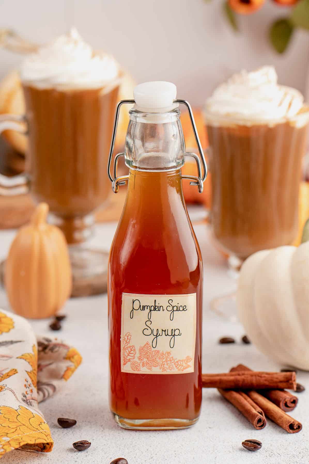 pumpkin spice syrup in a bottle with label and lattes in the background