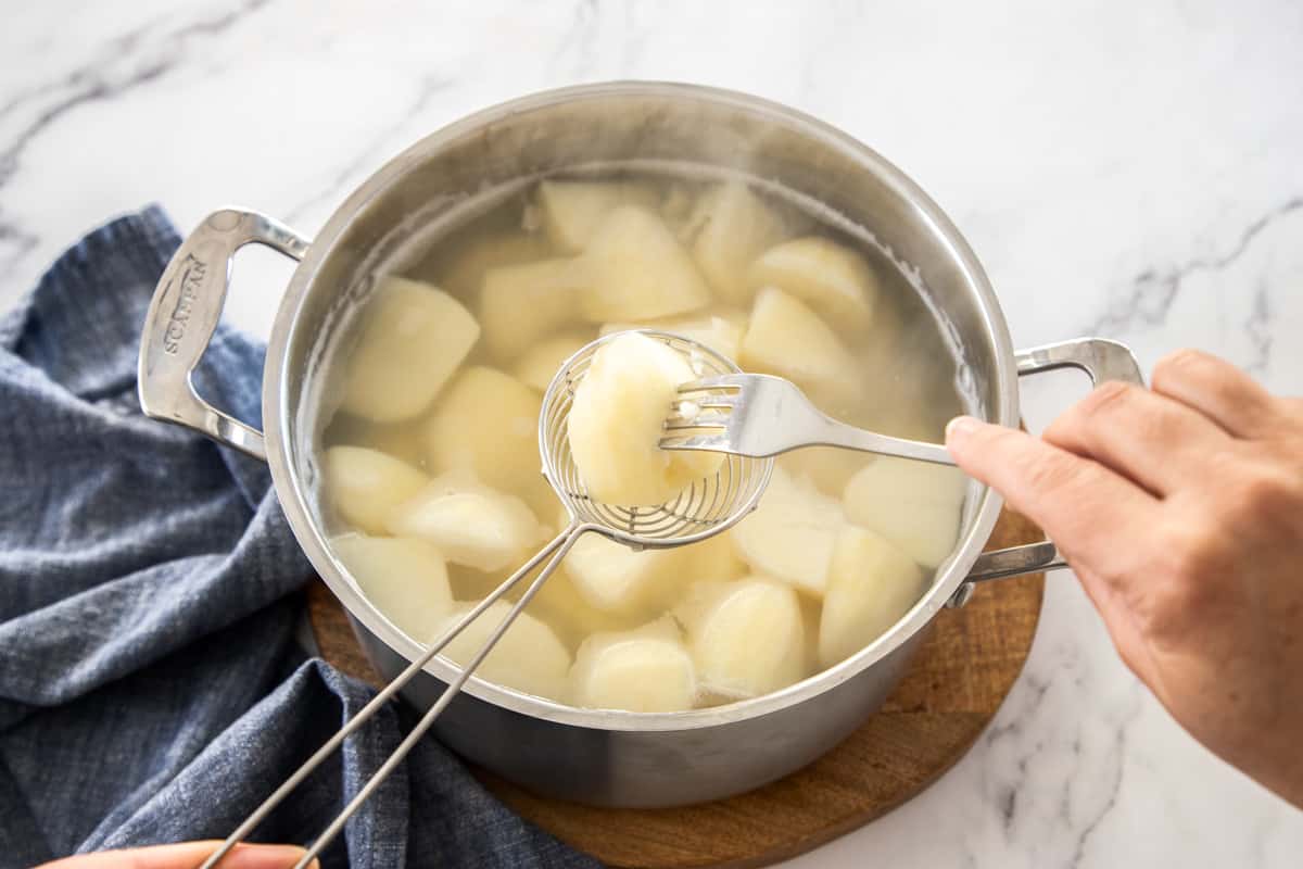 checking doneness of boiled potatoes in pot with fork