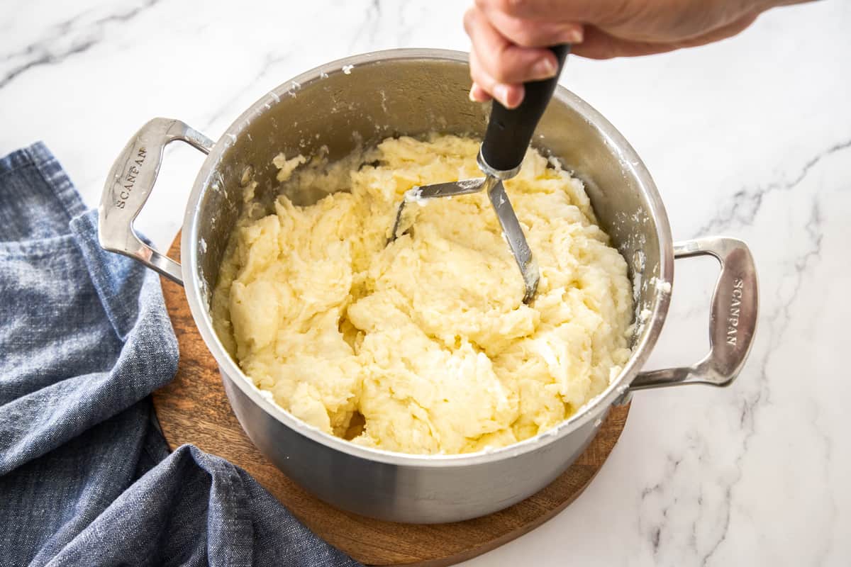 mashing potatoes in large pot with potato masher