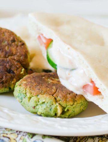 two falafels on a plate with pita bread and yogurt sauce