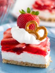 a serving of strawberry layered dessert garnished with cool whip and a whole strawberry and pretzel twist
