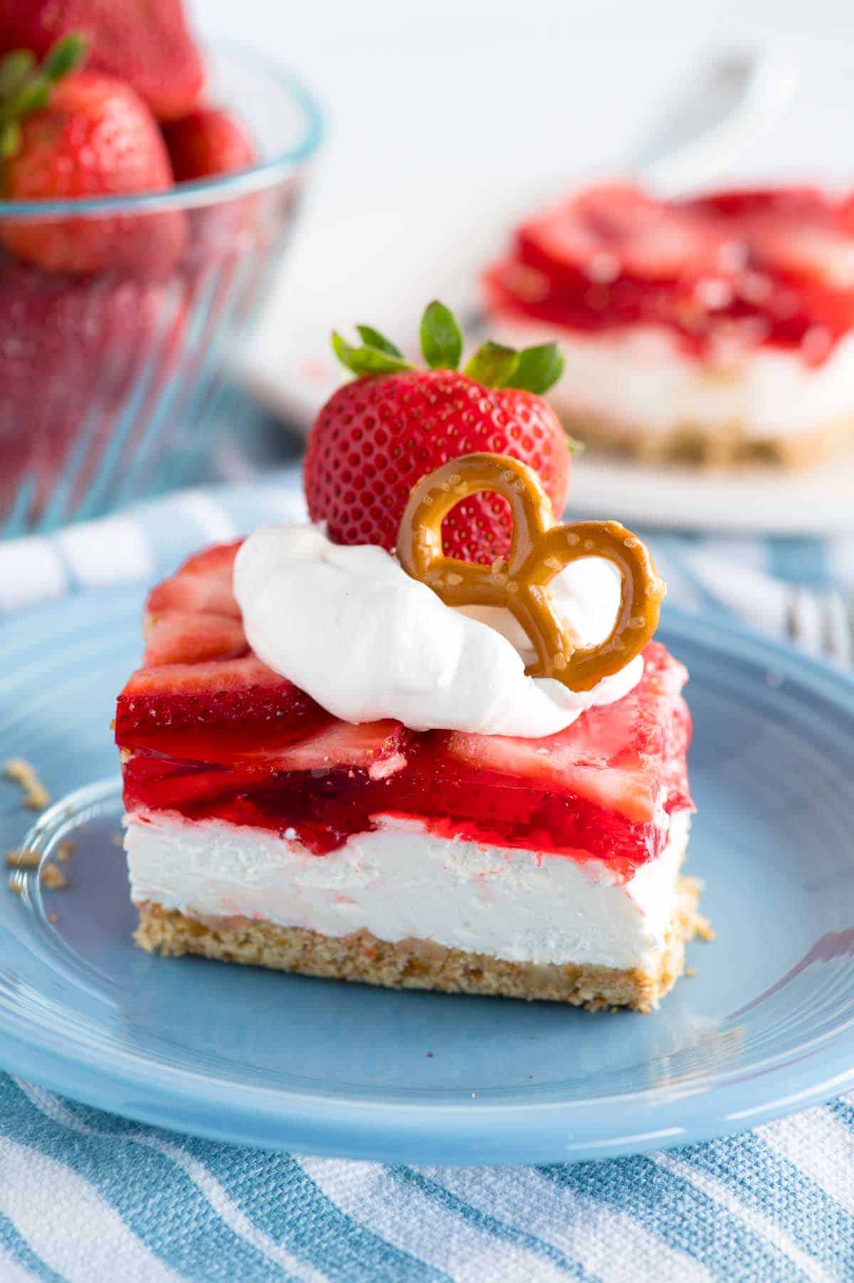 strawberry jello layered dessert on a plate garnished with whipped cream and a strawberry and twisted pretzel