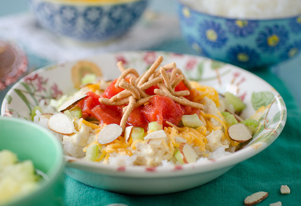 Landscape of Hawaiian Haystacks bowl of stacked rice, almonds, tomatoes and chow mein noodle.
