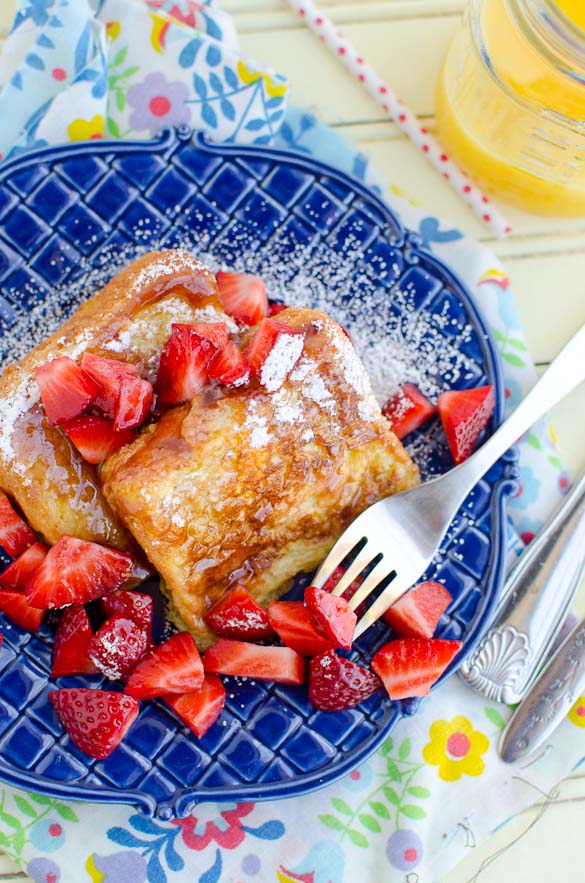 Overhead photo of Angel Food Cake French Toast with strawberries and syrup, a fork and blue plate.