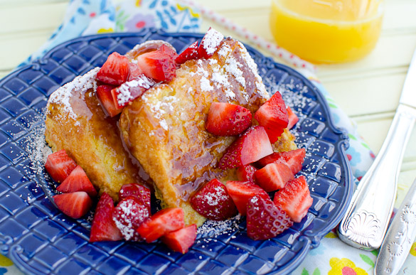 Slices of Angel Food Cake French Toast with strawberries and syrup on a blue plate.