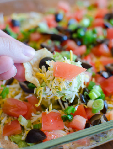 Seven Layer Dip Recipe - The easiest and quickest Mexican dip recipe with layers of refried beans, guacamole, taco seasoned sour cream and more!