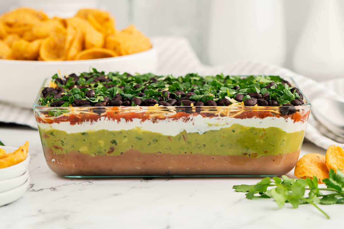 clear casserole dish with 7 layers of guacamole and sour cream and salsa