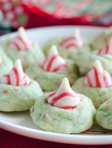 Sugar Cookie Candy Cane Blossoms are peppermint sugar cookies topped with Hershey's Candy Cane Kisses. They are a spin-off of the traditional peanut butter kiss blossoms. You will love these Candy Cane Blossom cookies because they are easy to make, delicious to eat, and perfect for your Christmas cookie swap!