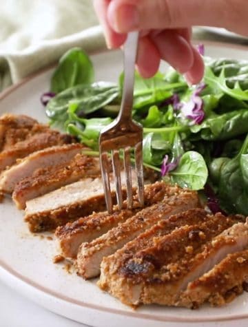 sliced almond crusted pork on a plate with salad greens