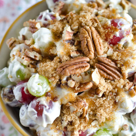 A bowl of red and green grape salad topped with pecans and brown sugar