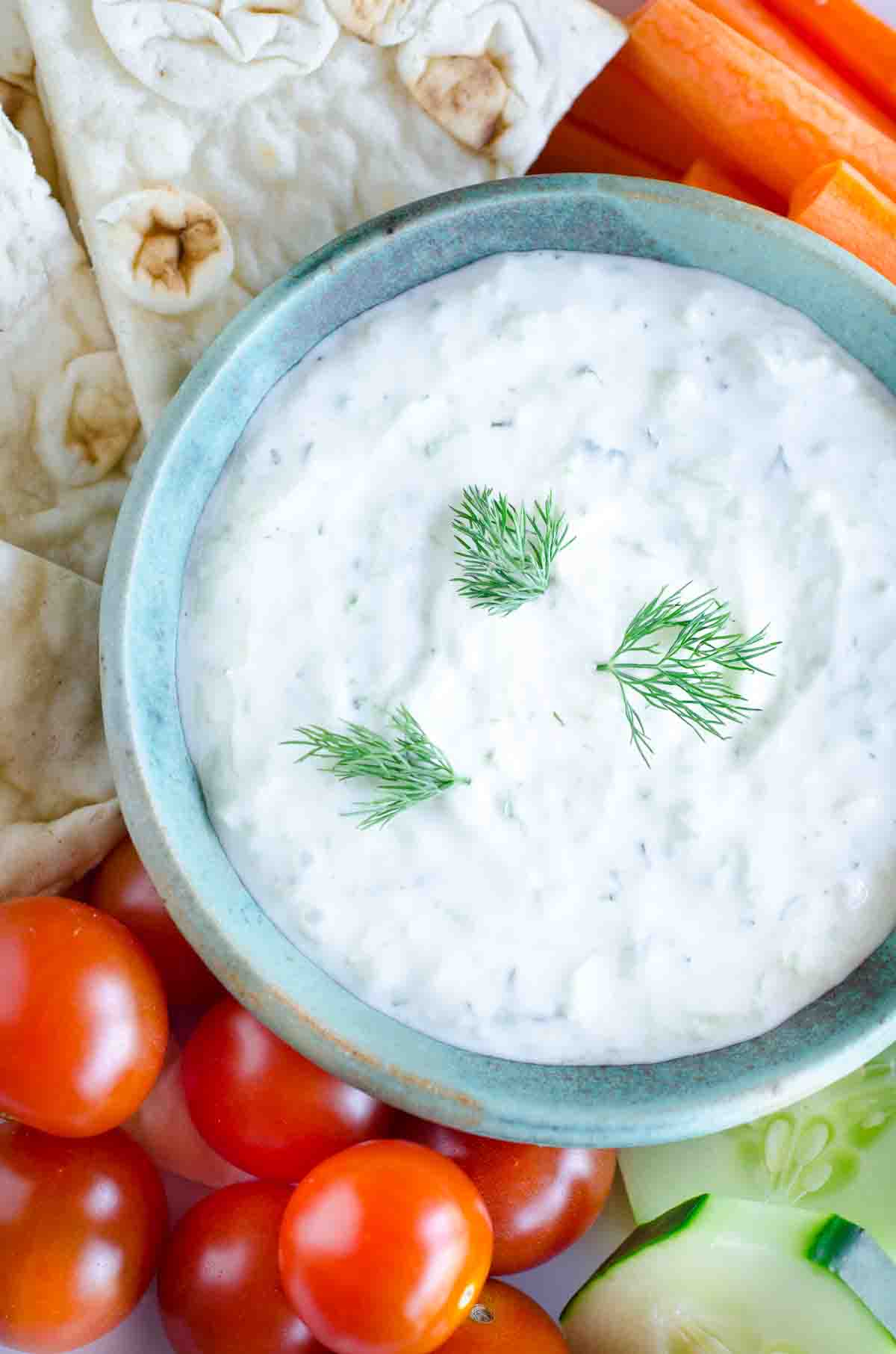 tzatziki in a bowl with tomatoes and pita and veggies