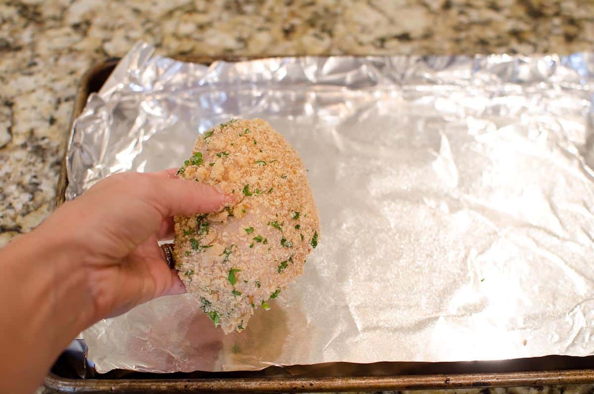 placing coated chicken breast on foil lined baking sheet