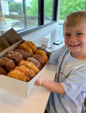 Little boy holding box of donuts.