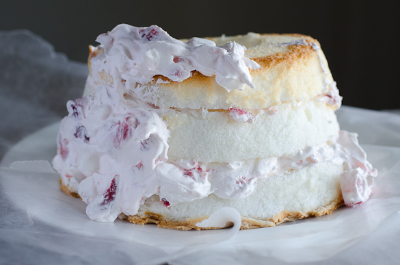Frosting a layered angel food cake with strawberry marshmallow whipped topping.