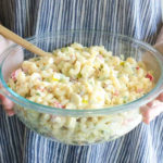 holding a glass bowl full of macaroni salad