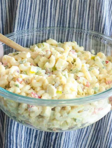 holding a glass bowl full of macaroni salad