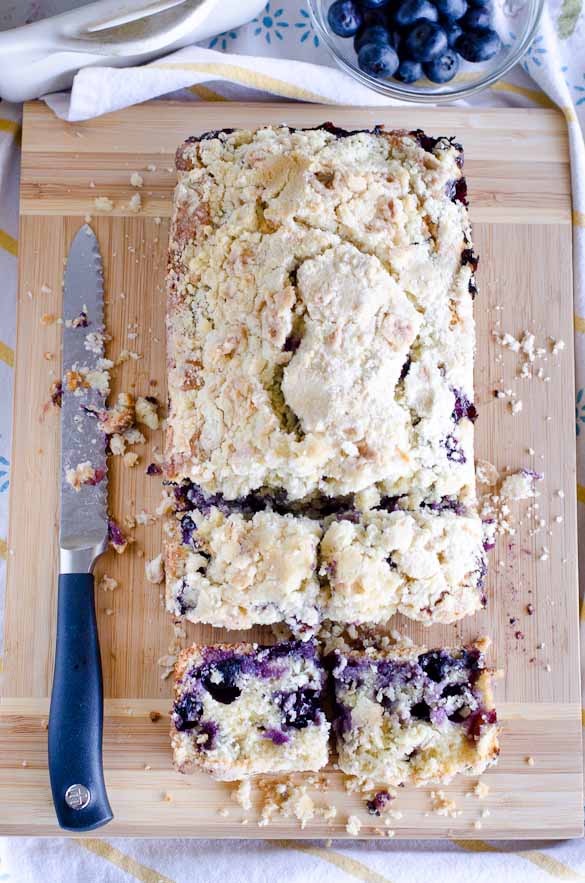 Loaf of blueberry muffin bread with knife on cutting board.