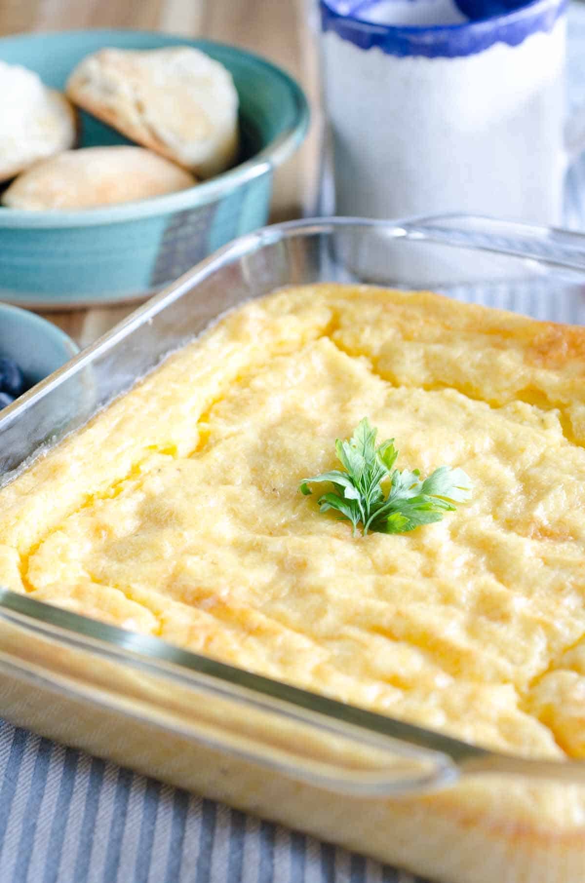 square pan of cheese grits casserole with biscuits in background