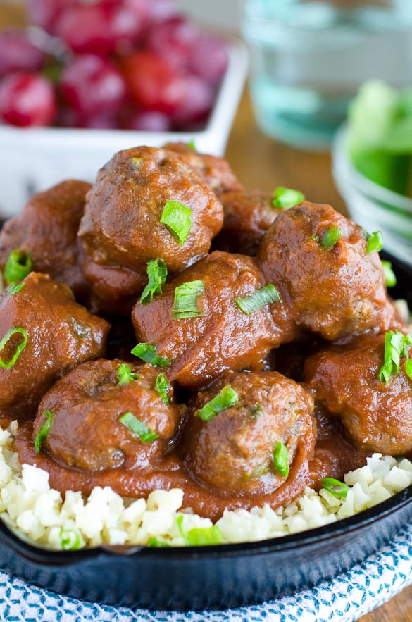 Meatballs stacked in a skillet over rice with grapes in the background