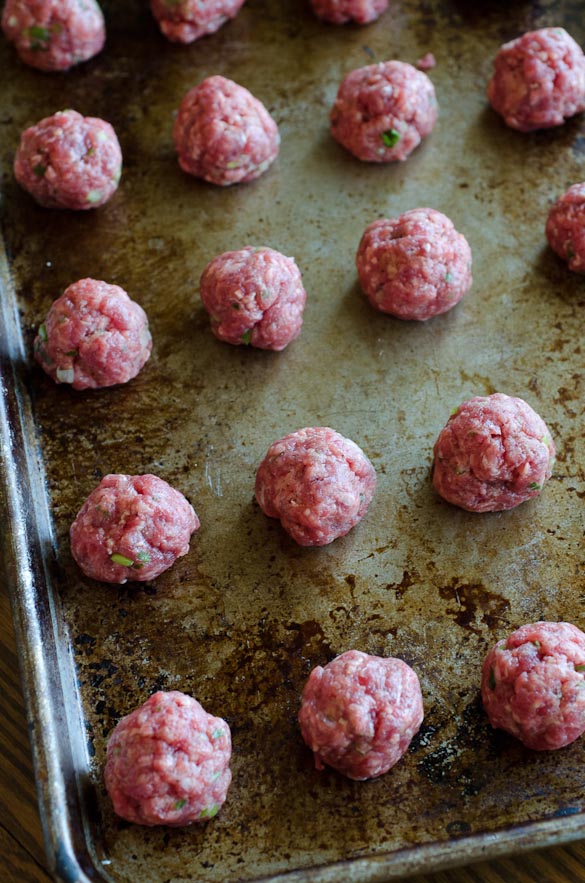 Uncooked meatballs lined on baking sheet