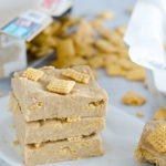 Stack of homemade protein bars topped with Chex cereal and cereal spilled in the background