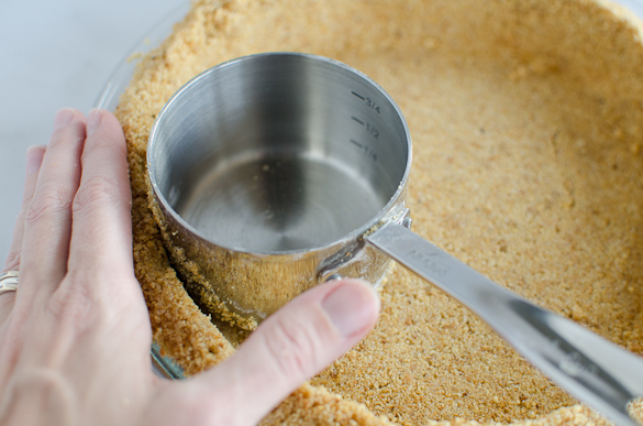 using measuring scoop to press graham cracker crust into pie plate