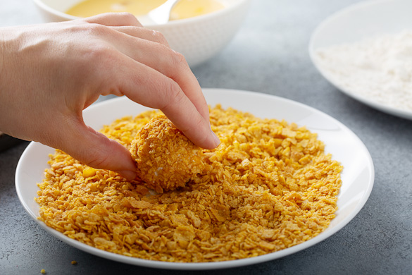 dipping chicken bite into cornflakes coating