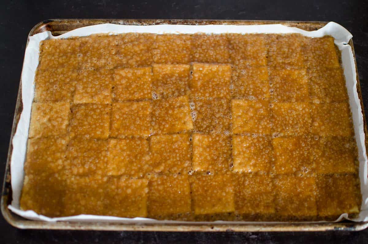 hot toffee mixture layered over saltine crackers lined in rimmed baking sheet