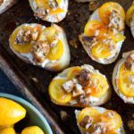 crostini on a baking sheet topped with kumquat slices, ricotta and honey walnuts