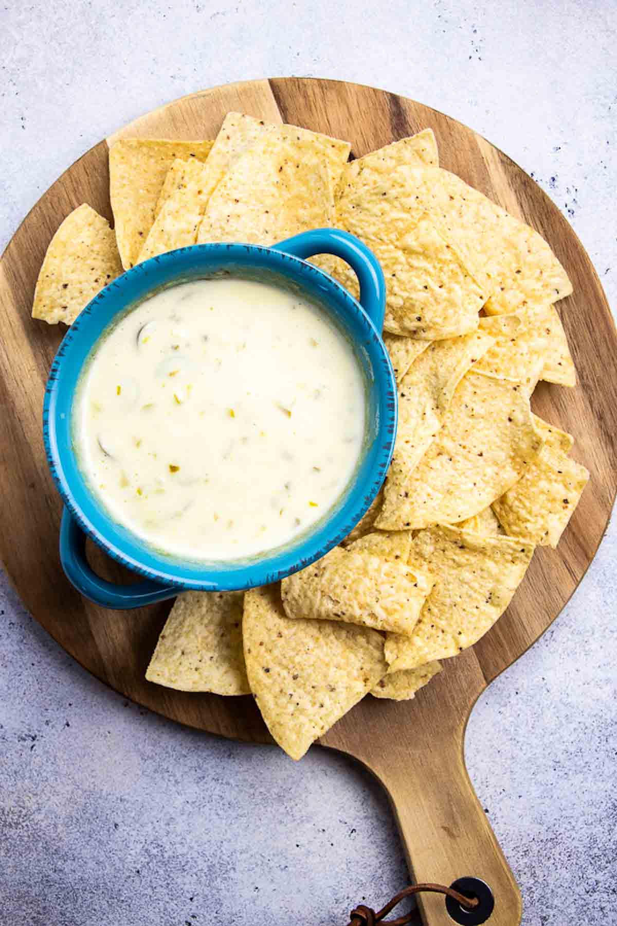 overhead shot of tortilla chips and cheese dip on a wooden serving platter 