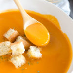 spoon in a bowl of tomato soup with croutons