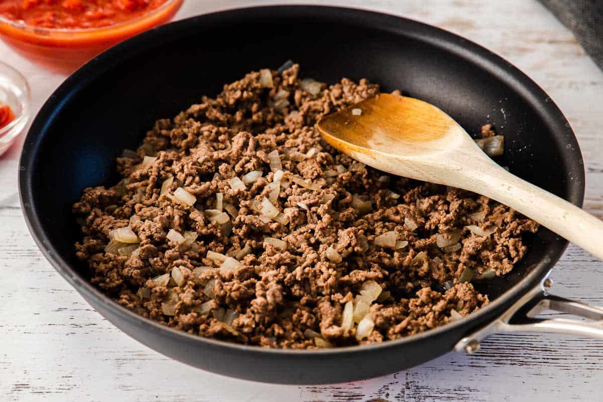 browning ground beef in skillet with wooden spoon