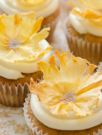 dried pineapple flowers topped onto cupcakes with vanilla frosting
