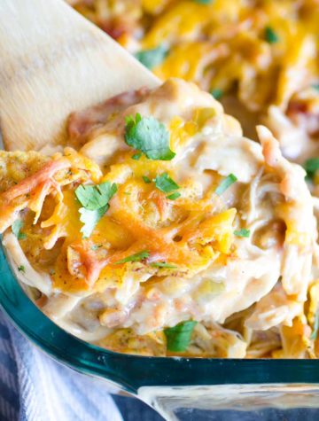 wooden spoon scooping cheesy dorito chicken casserole out of baking dish
