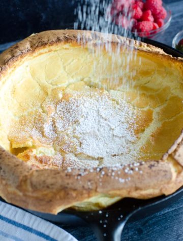 puffy dutch baby in cast iron skillet sprinkled with powdered sugar