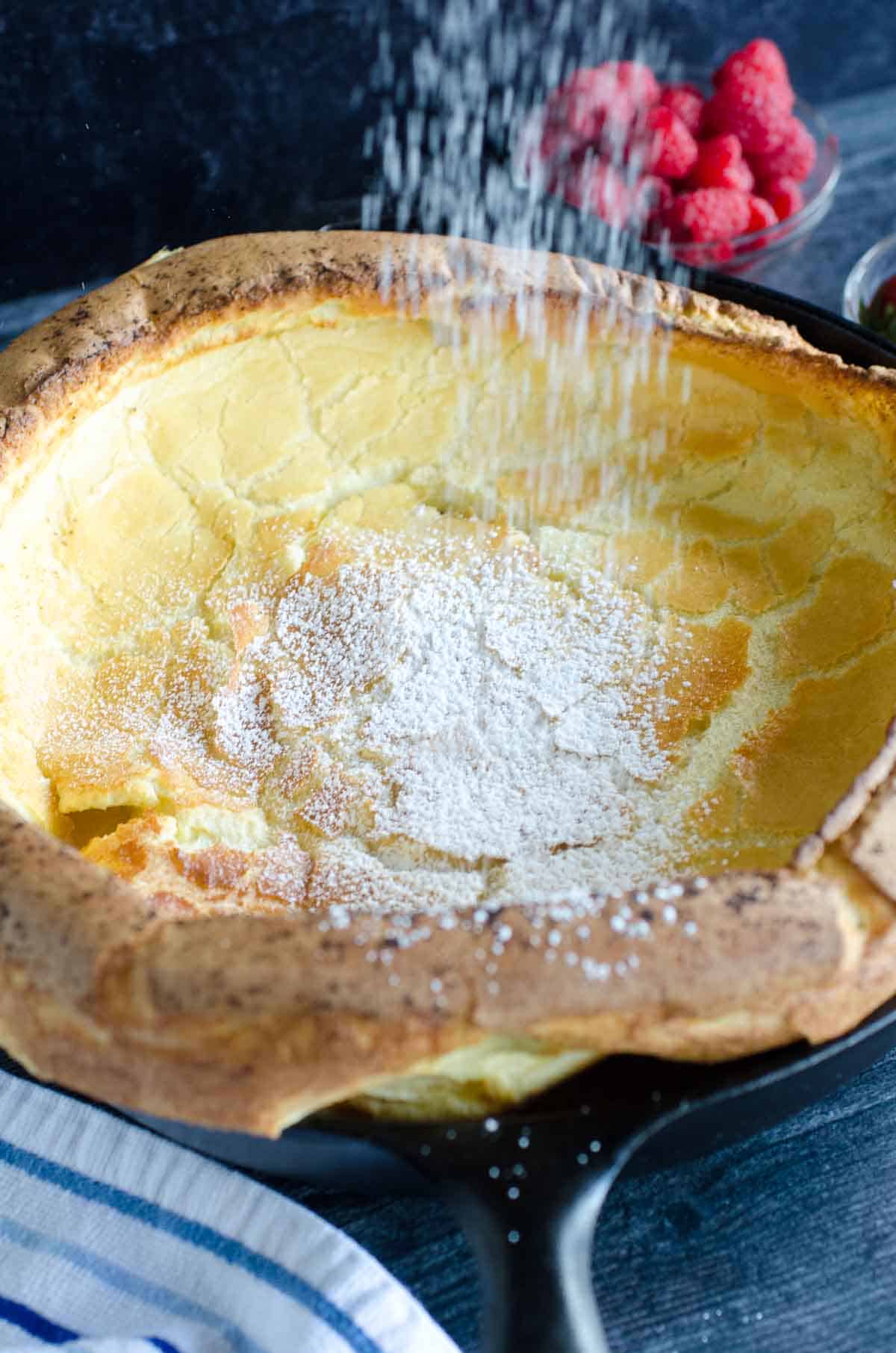 powdered sugar sprinkling over german pancake in cast iron skillet