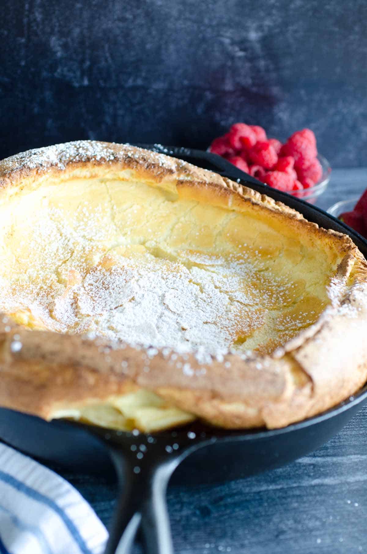 dutch baby pancake in cast iron skillet dusted with powdered sugar