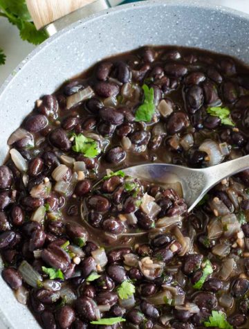 spoon scopping into skillet of mexican black beans with cilantro