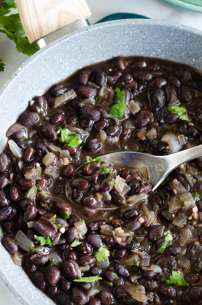 spoon scopping into skillet of mexican black beans with cilantro
